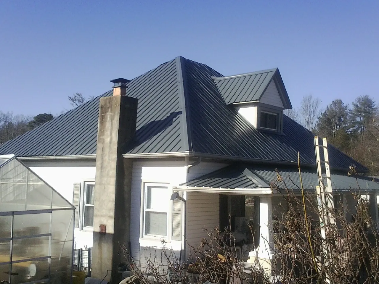 Dark blue standing seam metal roof on a white farmhouse with dormer — Slate & Tile Roof Repair by Roofing Brothers in Liberty Hill