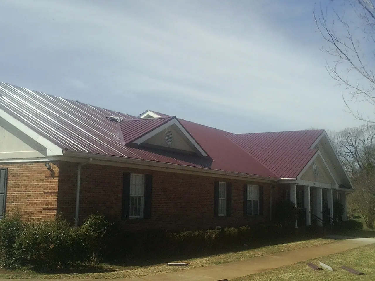 Red metal roof with gabled entries on a long brick building, from a Hail Damage Roof Repair job in Liberty Hill