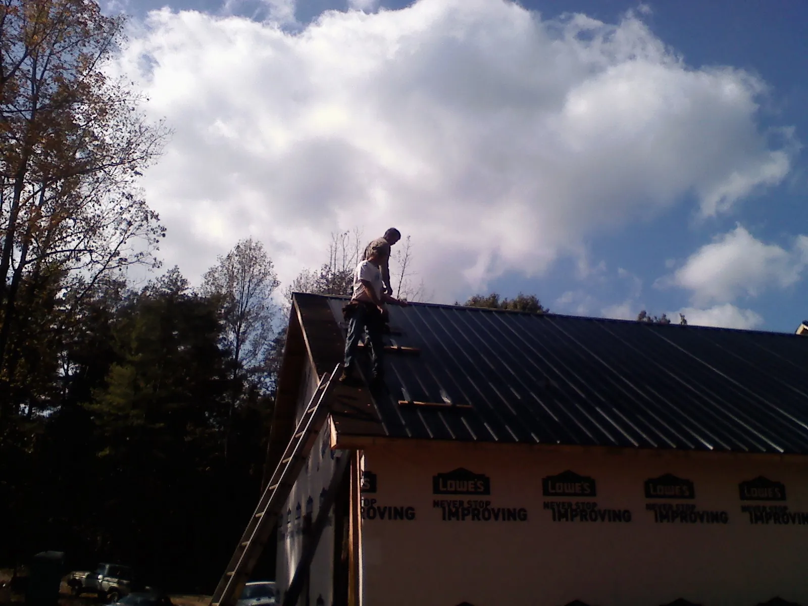 Roofer fastening dark metal panels high against a cloudy sky, from a Roof Inspection job in Liberty Hill