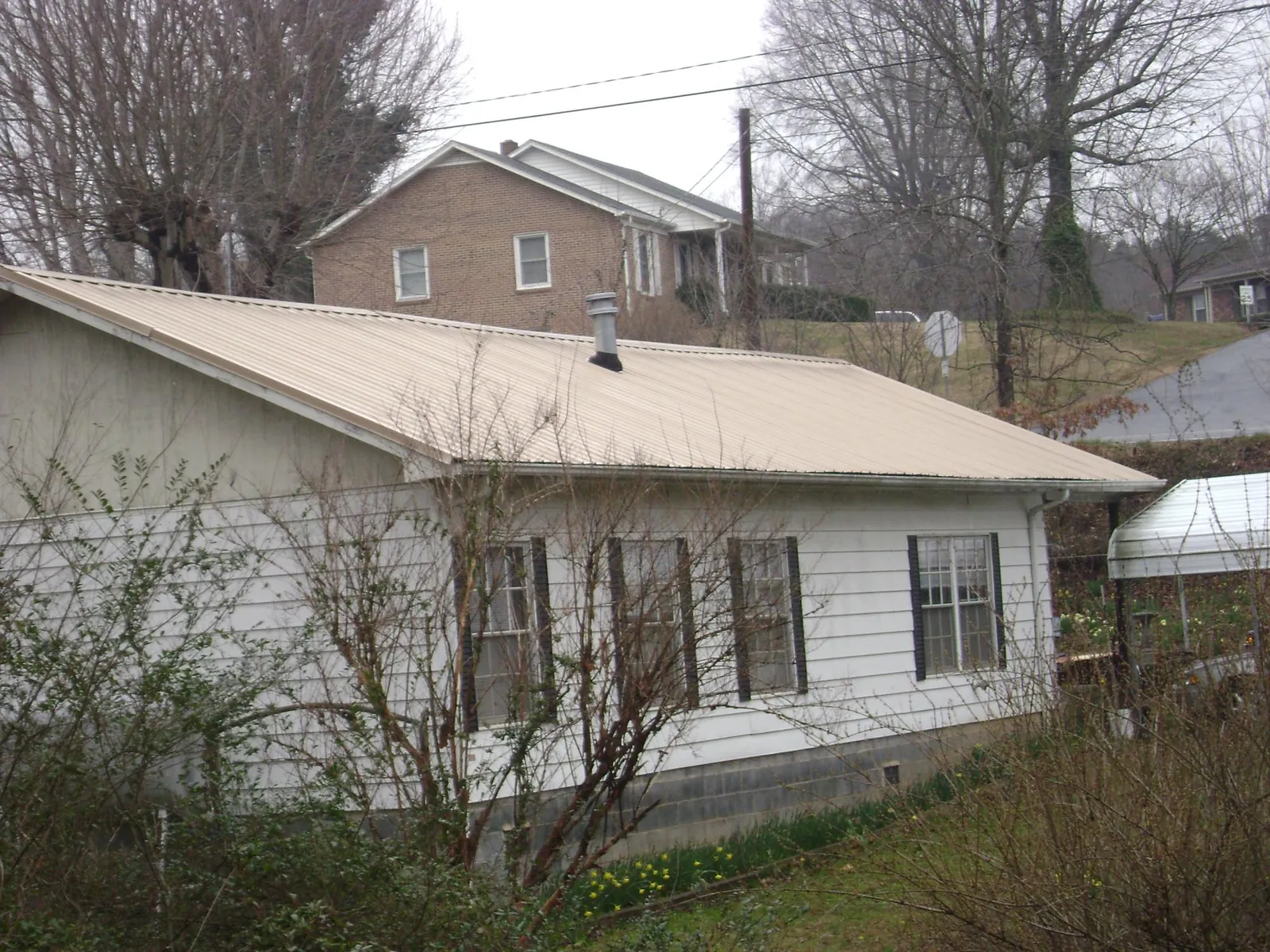 Tan metal roof on a white sided house set into a hillside — Commercial Roofing by Roofing Brothers in Liberty Hill
